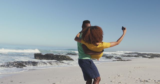Happy biracial couple walking on beach, hugging and doing selfie - Download Free Stock Photos Pikwizard.com