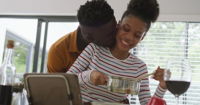 Image of happy african american couple embracing while cooking together in kitchen. love relationship, togetherness and spending quality time at home. .