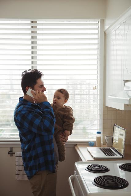 Father talking on mobile phone while holding his baby - Download Free Stock Photos Pikwizard.com