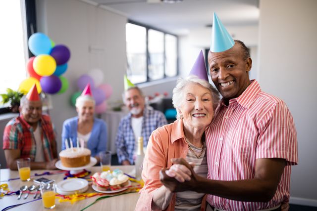 Portrait of senior couple standing by table during birthday party with friends in background