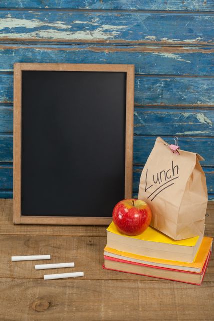 Slate, chalk, apple, lunch bag and books against blue wooden background