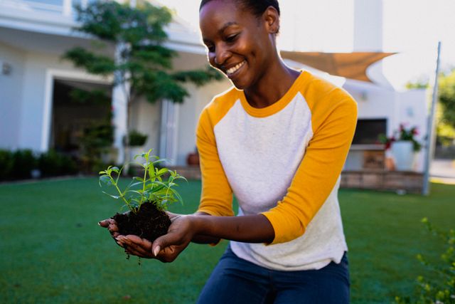 Smiling african american woman holding plant seedling in garden - Download Free Stock Photos Pikwizard.com