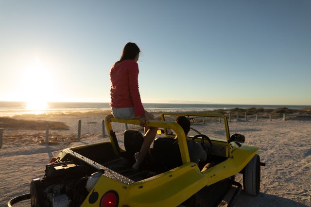 Happy caucasian couple driving in beach buggy by the sea at sunset, woman sitting on roll bar - Download Free Stock Photos Pikwizard.com