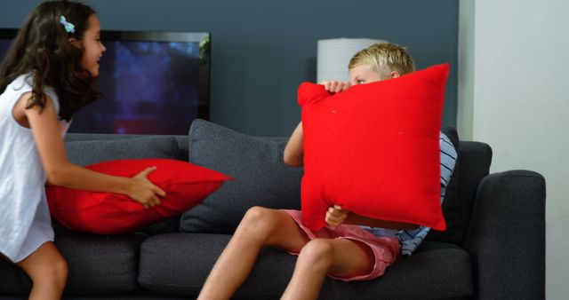 A young girl and boy are having a playful pillow fight in a living room, with copy space - Download Free Stock Photos Pikwizard.com