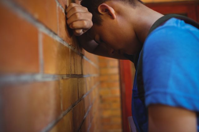 Sad schoolboy leaning on brick wall - Download Free Stock Photos Pikwizard.com