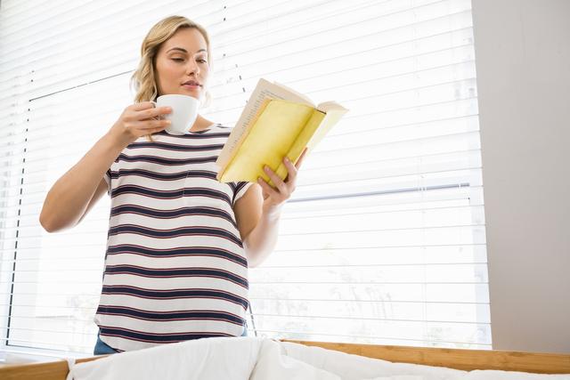 Beautiful woman holding coffee cup and reading book - Download Free Stock Photos Pikwizard.com