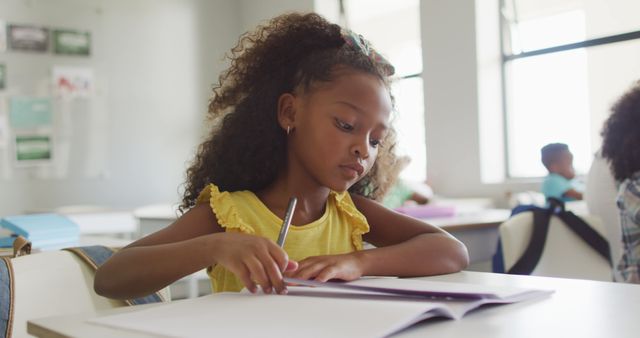 Image of focused african american girl sitting at desk during lesson in classroom. primary school education and learning concept.