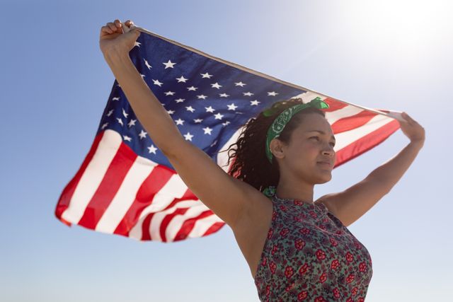 Low angle view of beautiful young woman waving american flag on beach in the sunshine