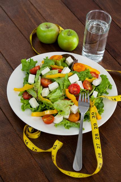 Salad, apple and measuring tape on table - diet concept