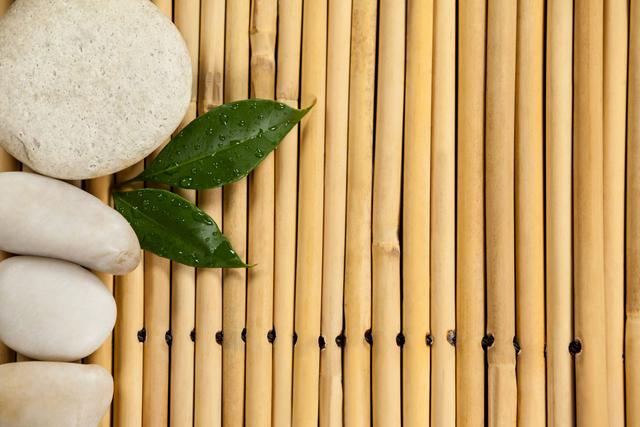Two green leaves and four white stones on the bamboo mat - Download Free Stock Photos Pikwizard.com
