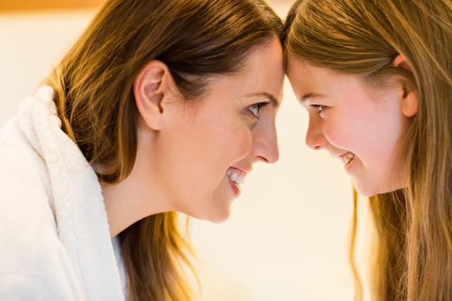 Happy mother and daughter looking at each other in bedroom at home