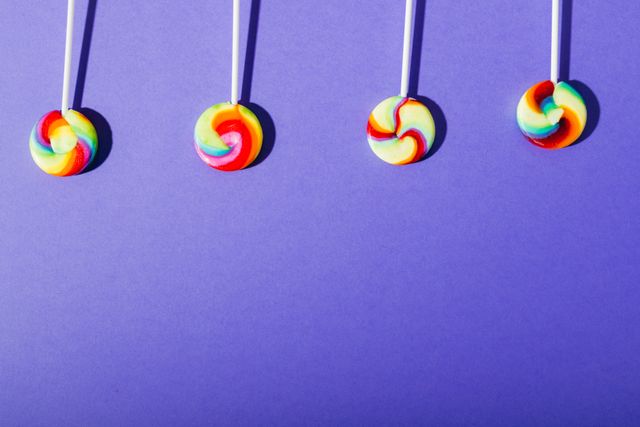 Overhead view of swirl pattern colorful lollipops side by side over copy space on blue background. unaltered, unhealthy eating and sweet food concept.
