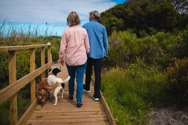 Rear view of senior caucasian couple walking with their dogs on a bridge outdoors. cob home living and lifestyle concept