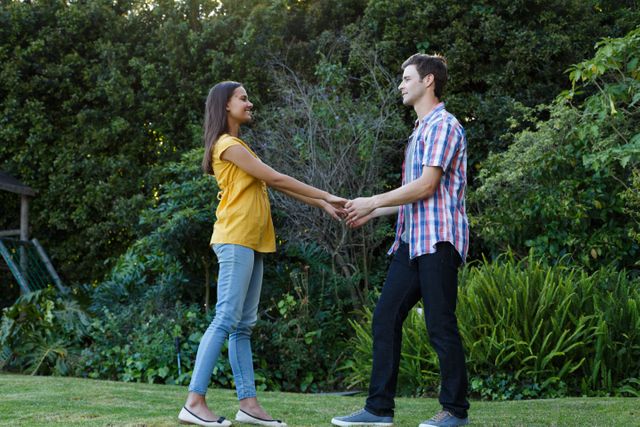 Mixed race woman and caucasian man holding hands in garden looking at each other smiling - Download Free Stock Photos Pikwizard.com