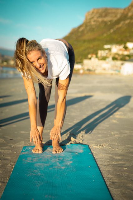 Happy caucasian woman stretching on beach and looking at camera - Download Free Stock Photos Pikwizard.com