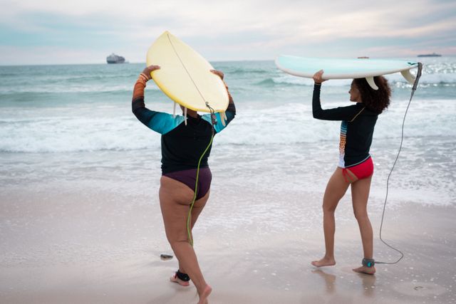 Back view of two diverse female friends holding surfboards at sea - Download Free Stock Photos Pikwizard.com