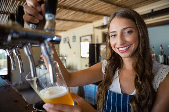 Portrait of smiling barmaid pouring beer from tap in glass - Download Free Stock Photos Pikwizard.com