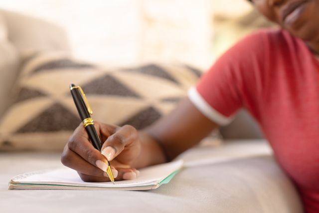 Midsection of african american young woman writing on notepad in living room at home, copy space. Unaltered, people, lifestyle and home concept.