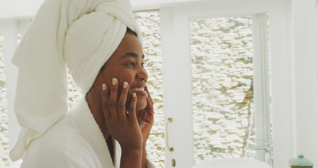 Image of happy african american woman moisturizing face. beauty treatment and skin care routine concept.