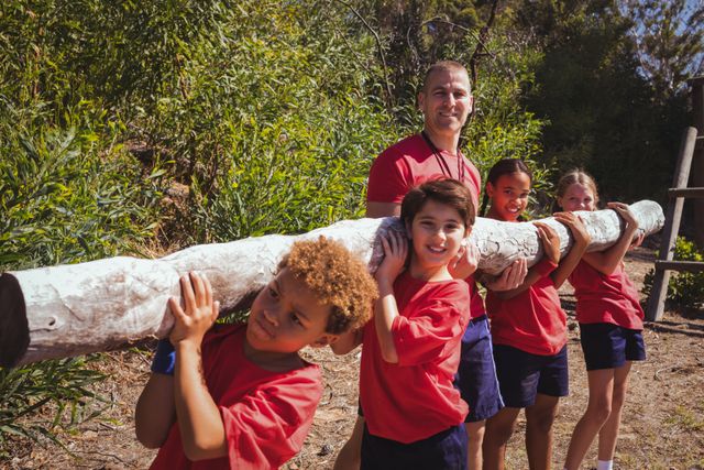 Trainer assisting kids in carrying a heavy wooden log during obstacle course training - Download Free Stock Photos Pikwizard.com