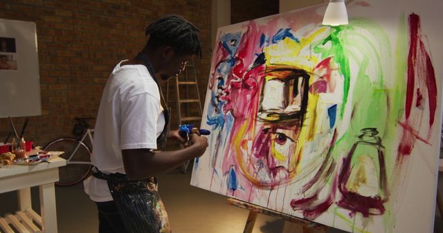 African american male artist wearing apron painting with palette knife on canvas at art studio. art, hobby and creative occupation concept
