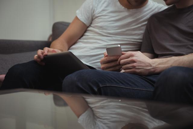 Gay couple sitting on sofa and looking at digital tablet - Download Free Stock Photos Pikwizard.com