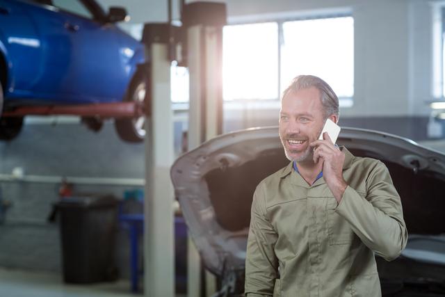 Smiling mechanic talking on a mobile phone in repair shop
