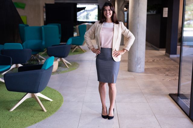Portrait of happy caucasian businesswoman standing with hands on hips in office lobby smiling. business, working at a modern office.