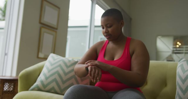 Happy african american plus size woman practicing yoga, using smartwatch in living room. healthy lifestyle, enjoying leisure time at home.