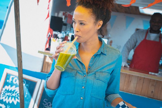 Happy mixed race woman enjoying takeaway health drink standing beside food truck. small independent business, street food, service and catering.
