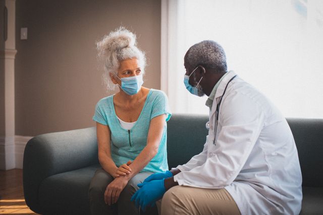 African american senior male doctor talking to female patient at home both wearing face masks - Download Free Stock Photos Pikwizard.com