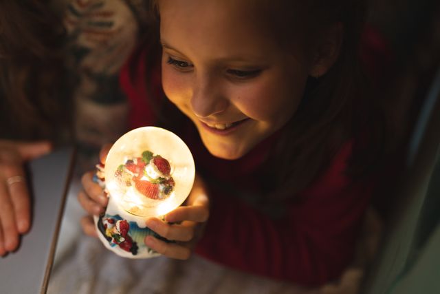 Caucasian girl holding a glowing christmas globe close to her face while smiling inside a blanket fo - Download Free Stock Photos Pikwizard.com