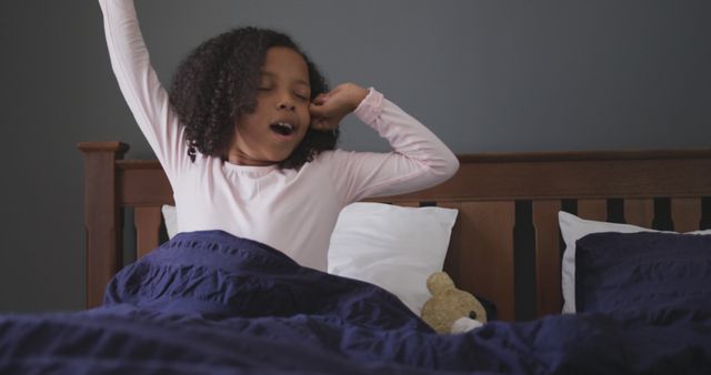 Happy african american girl waking up in the morning and stretching in bed at home. Childhood, health and domestic life.