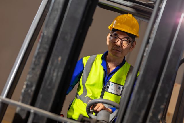 Portrait of asian mature male warehouse worker wearing eyeglasses and hardhat driving forklift - Download Free Stock Photos Pikwizard.com