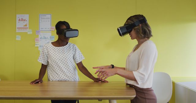 Two diverse female coworkers standing at desk, testing vr googles. independent creative business at a modern office.
