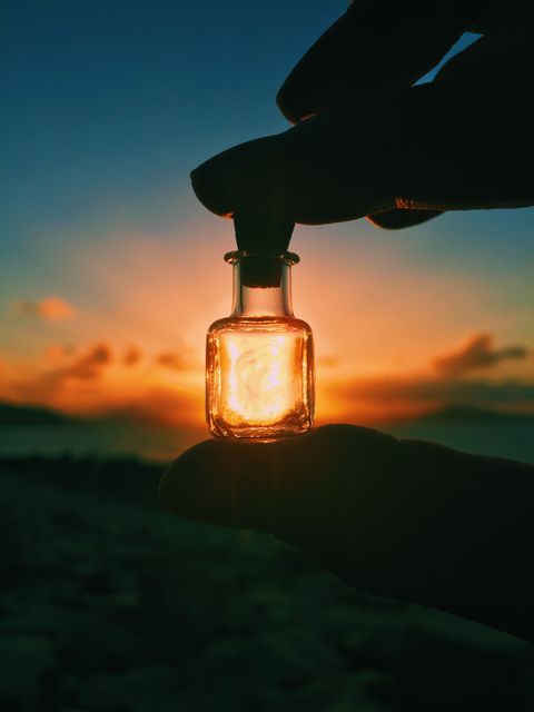 a person holding a small bottle with a small flame inside - Download Free Stock Photos Pikwizard.com