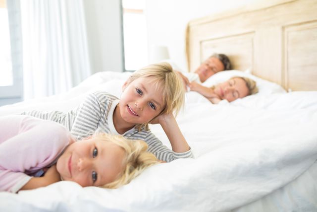 Smiling kids relaxing on bed while parents sleeping in background  - Download Free Stock Photos Pikwizard.com