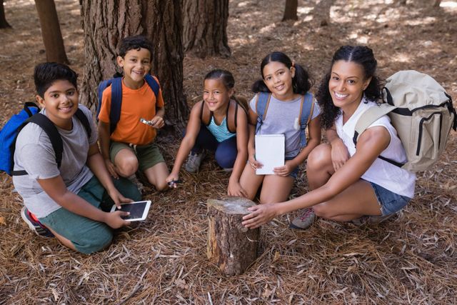 High angle portrait of teacher and students kneeling by tree stump in forest during field trip