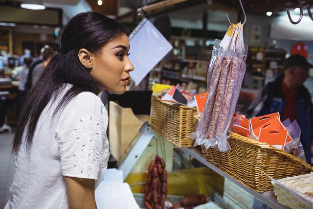 Thoughtful female staff standing at meat counter in supermarket