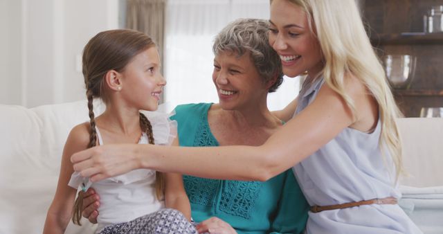 Happy caucasian grandmother, mother and daughter sitting on sofa, embracing and smiling. Lifestyle, domestic life, family, and togetherness.
