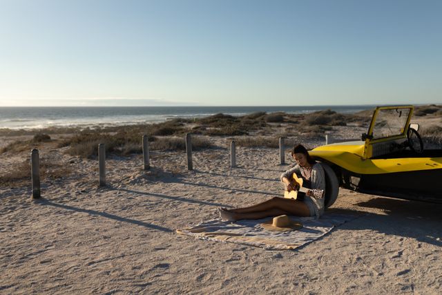 Caucasian man sitting on beach by beach buggy at sundown playing guitar - Download Free Stock Photos Pikwizard.com