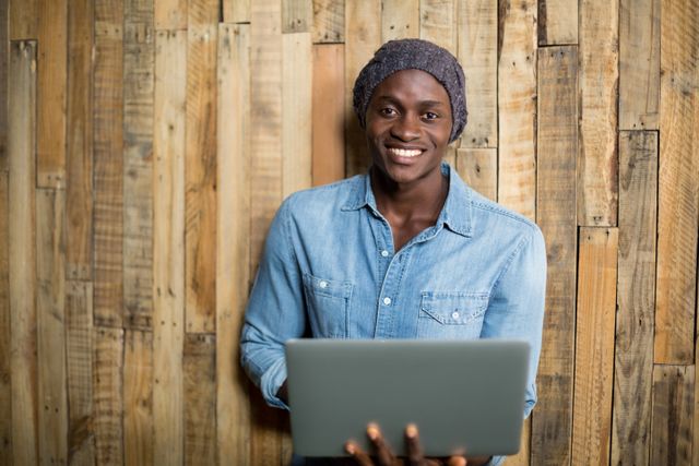 Smiling man using laptop against wooden wall - Download Free Stock Photos Pikwizard.com
