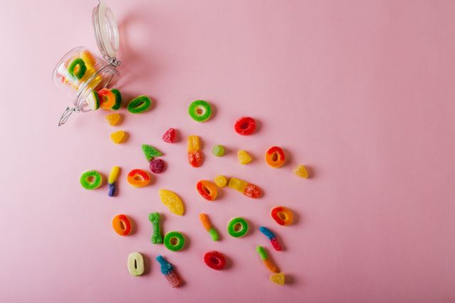Overhead view of scattered sugar candies by fallen glass jar and copy space on pink background. unaltered, unhealthy eating and sweet food concept.