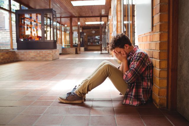 Sad schoolboy sitting alone in corridor - Download Free Stock Photos Pikwizard.com