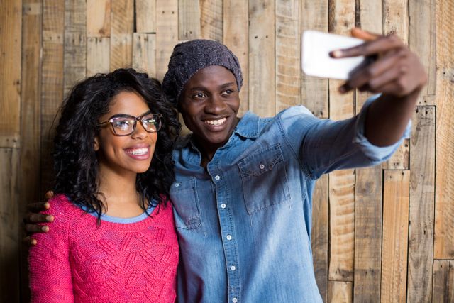 Couple taking a selfie from mobile phone against wooden wall - Download Free Stock Photos Pikwizard.com