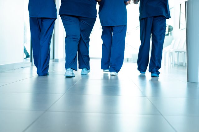 Low section of legs of female and male doctors wearing scrubs walking in hospital corridor. Medical services, hospital and healthcare concept.