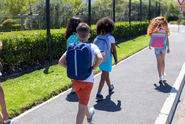Rear view of group of kids with backpacks walking on footpath - Download Free Stock Photos Pikwizard.com