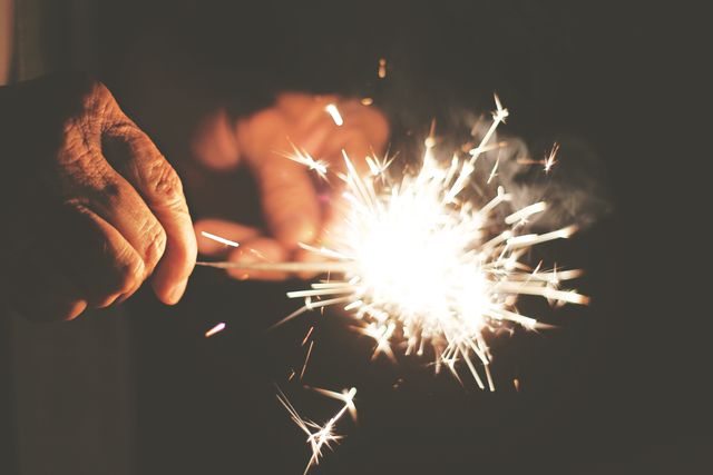 Close up view of a hand holding a burning sparkler against dark background. festivity and celebration concept
