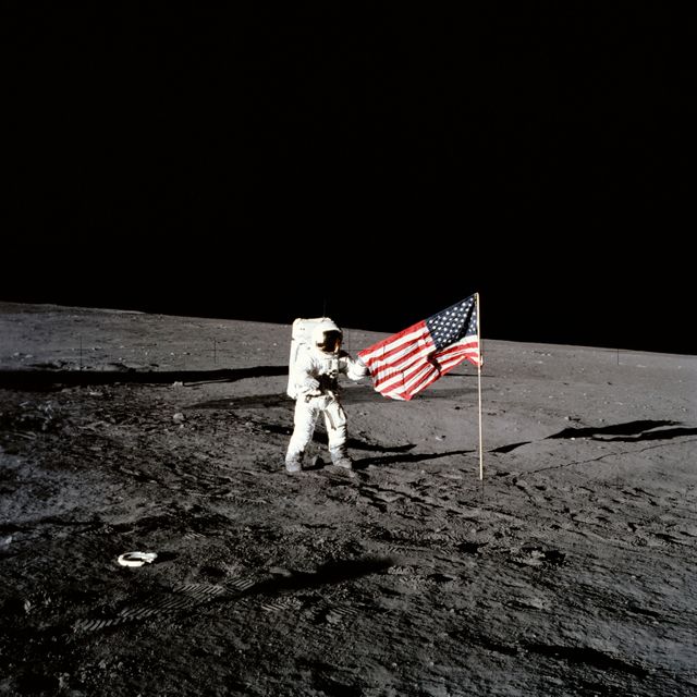 AS12-47-6897 (19 Nov. 1969) --- Astronaut Charles Conrad Jr., Apollo 12 commander, stands beside the United States flag after it was unfurled on the lunar surface during the first extravehicular activity (EVA), on Nov. 19, 1969. Several footprints made by the crewmembers can be seen in the photograph. While astronauts Conrad and Alan L. Bean, lunar module pilot, descended in the Lunar Module (LM) "Intrepid" to explore the Ocean of Storms region of the moon, astronaut Richard F. Gordon Jr., command module pilot, remained with the Command and Service Modules (CSM) "Yankee Clipper" in lunar orbit.
