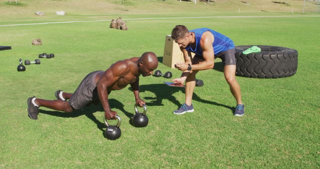 Two diverse fit men exercising outdoors, one doing push ups on kettlebells while the other times him - Download Free Stock Photos Pikwizard.com
